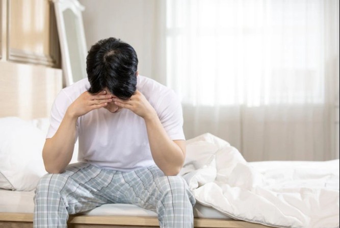 침대에서 머리를 감싸고 고민하는 남자